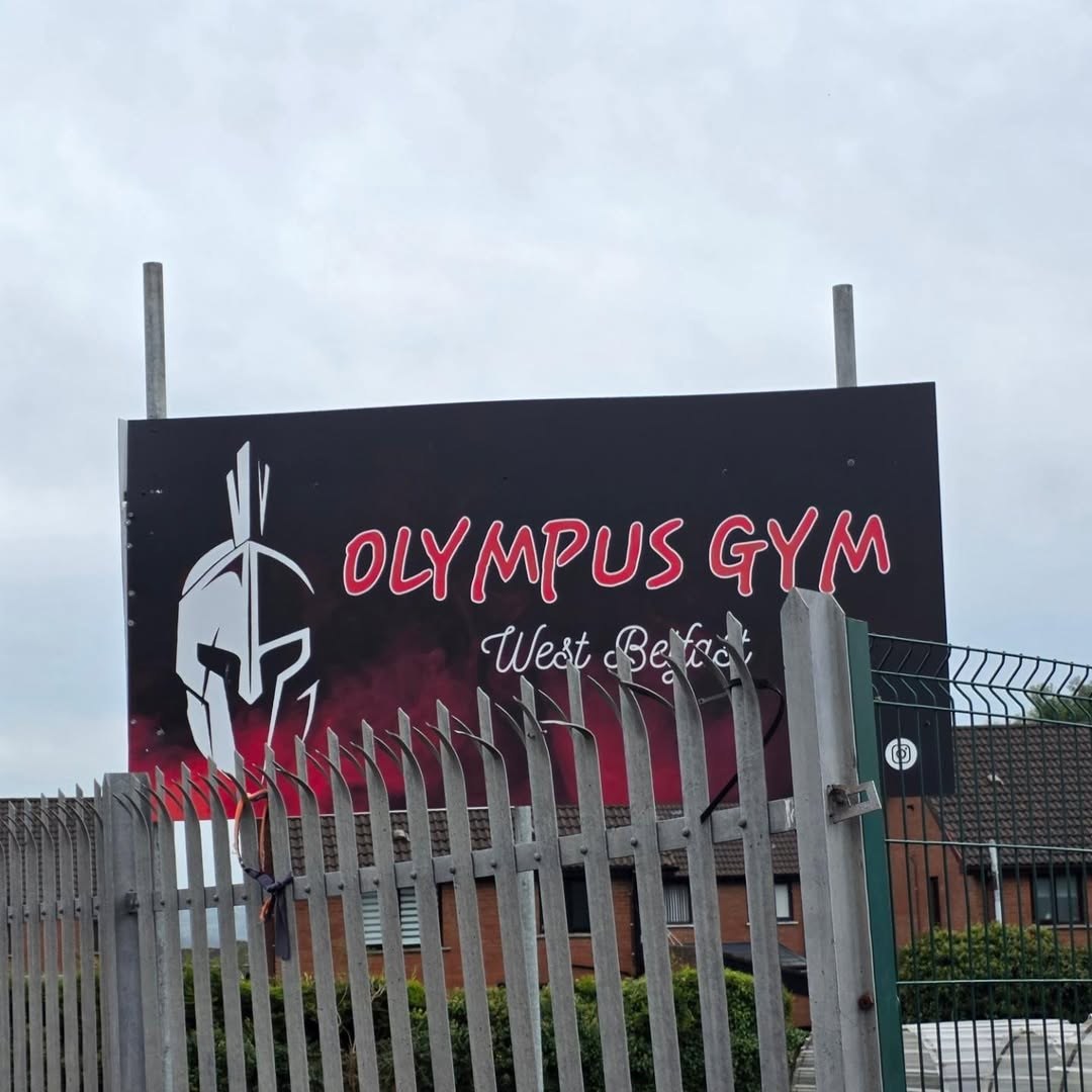 The large Olympus Gym West Belfast sign on the fence outside the gym