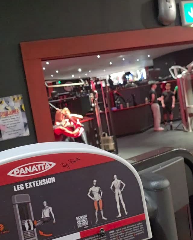 Dark gym interior with red-lit walls and a leg extension machine